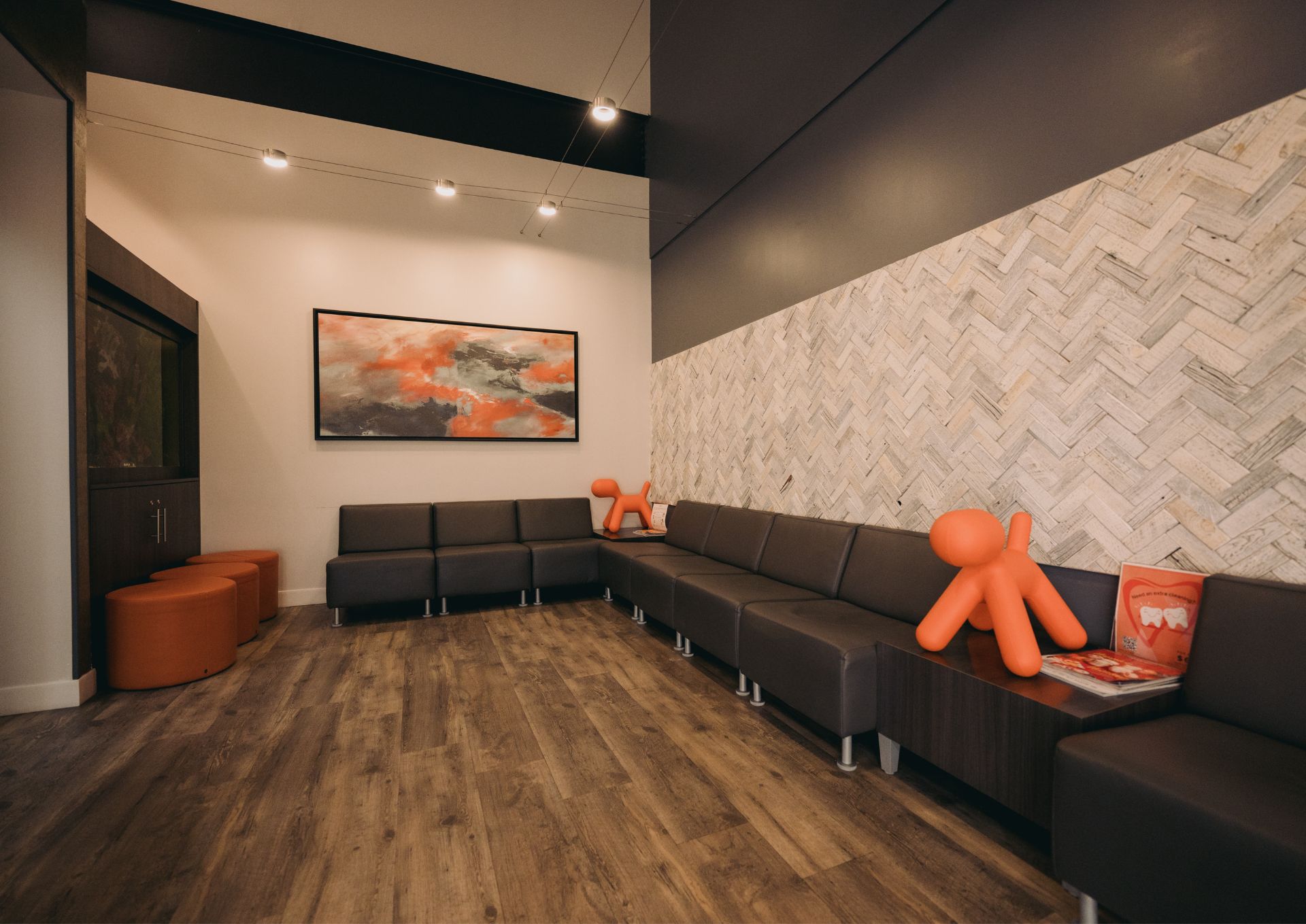 Modern waiting room with gray sectional seating, orange stools, decorative orange dog sculptures, and abstract wall art.