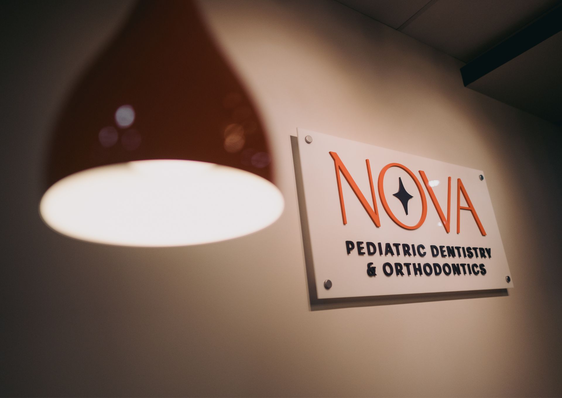 Wall-mounted sign reading 'NOVA Pediatric Dentistry & Orthodontics' with a modern ceiling light in the foreground.