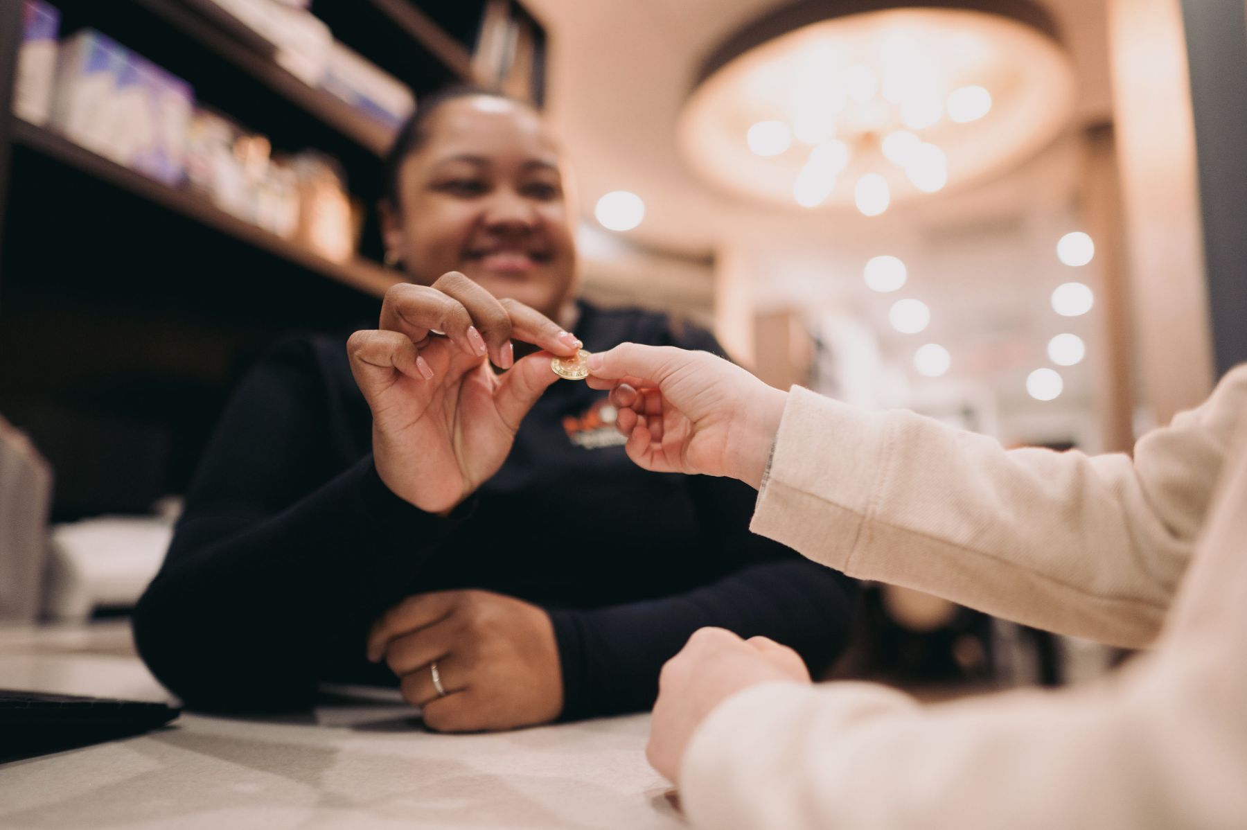 A person handing a coin to a smiling woman seated at a counter.