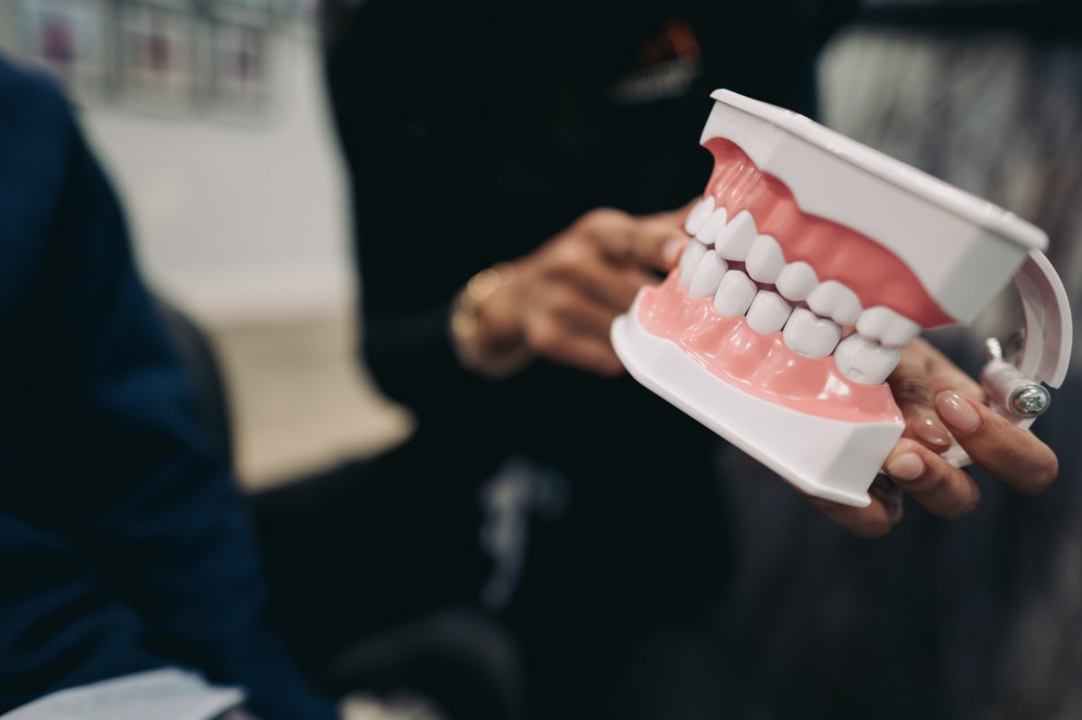 Dentist holding a dental model showing tooth structures and filling placement during patient consultation.