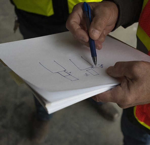 Person in a safety vest holding paper with hand-drawn geometric sketches and measurements.