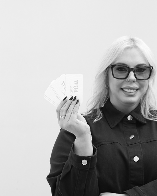 Woman with light hair and glasses holding four cards fanned out in her hand.