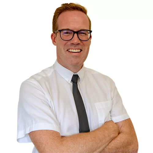 Smiling Colin with glasses wearing a white shirt and black tie, arms crossed.
