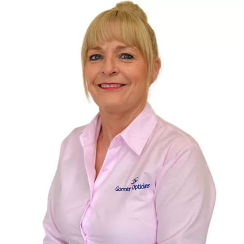 Smiling Michelle with blonde hair in a bun wearing a pink shirt embroidered with 'Gormey Opticians'.