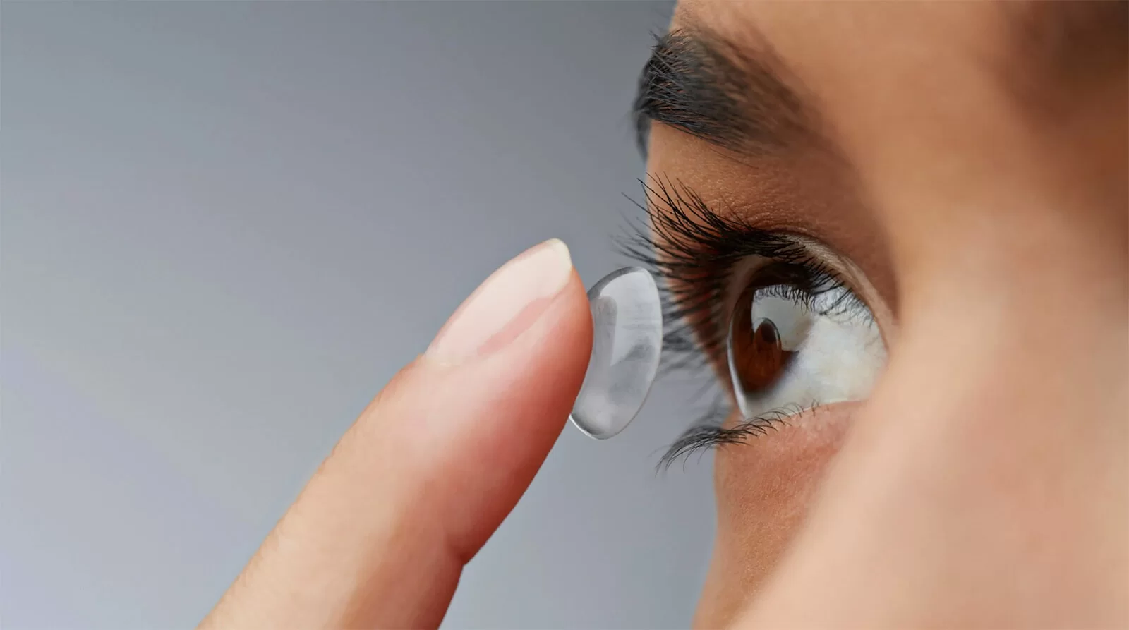 Close-up of a person holding a contact lens on their fingertip near their eye.
