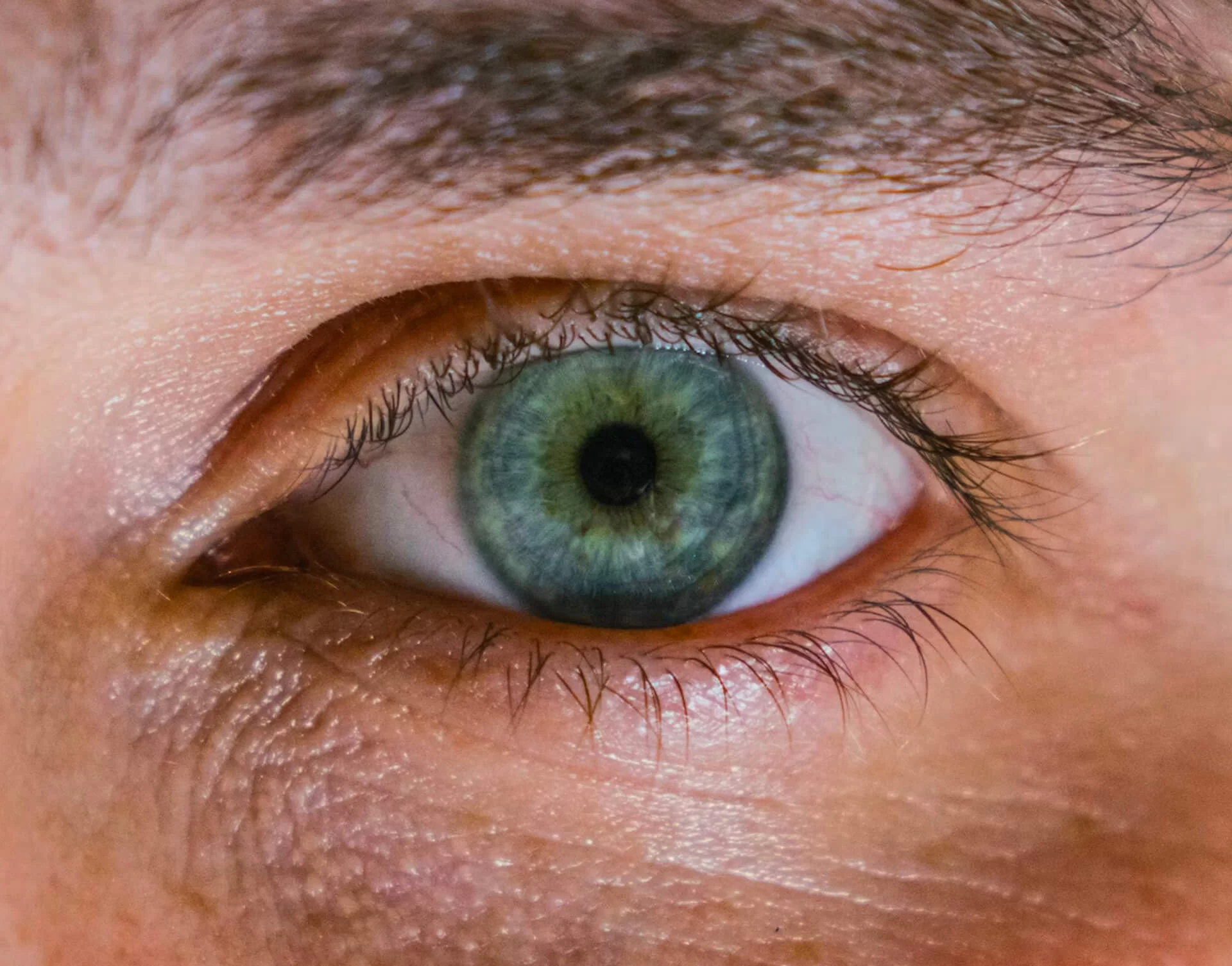 Close-up of a greenish-blue eye with visible iris patterns and surrounding skin texture.