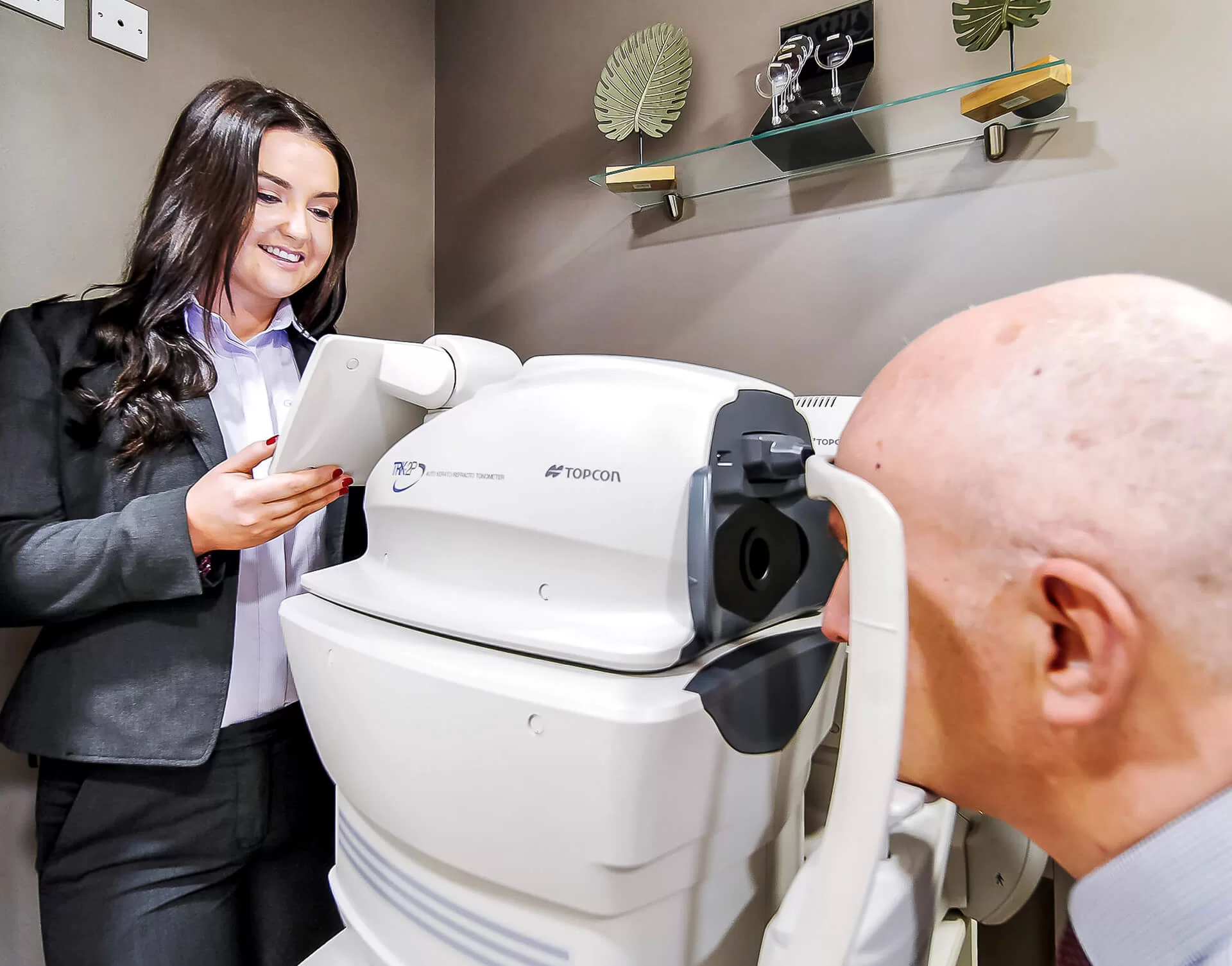Eye care professional conducting an eye test using a Topcon autorefractor with a patient positioned at the machine.