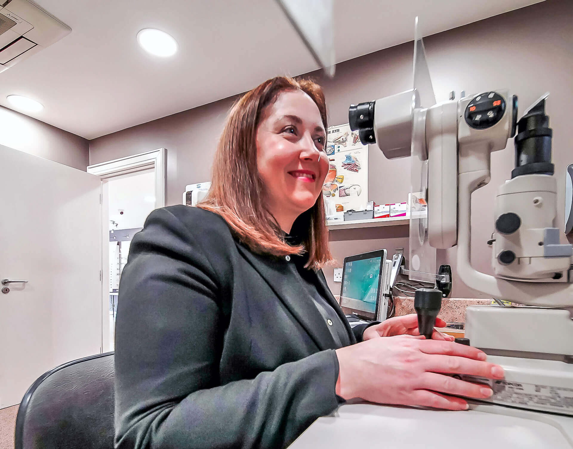 Woman sitting in an optometrist's office using a slit lamp for an eye examination.