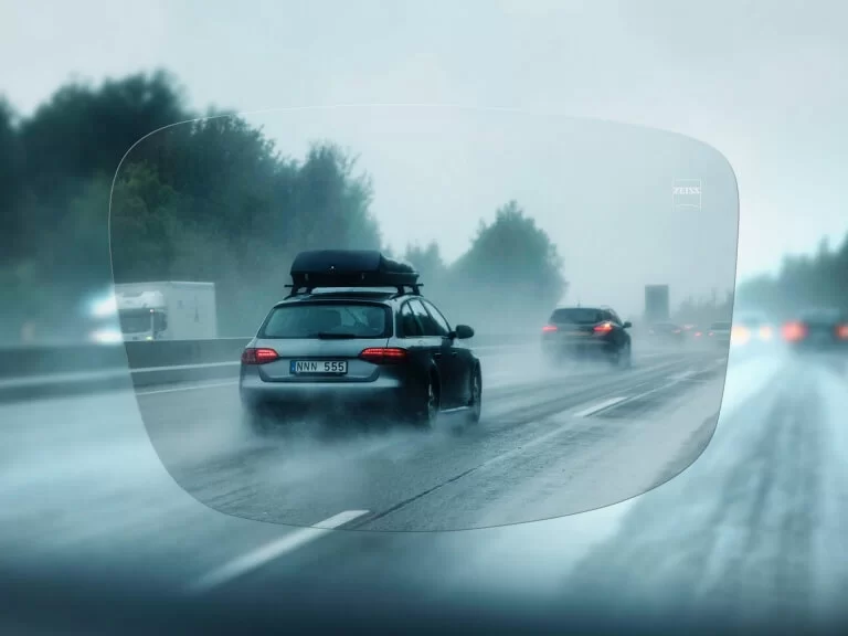 View through a clear eyeglass lens showing a wet highway with cars driving in rainy conditions.