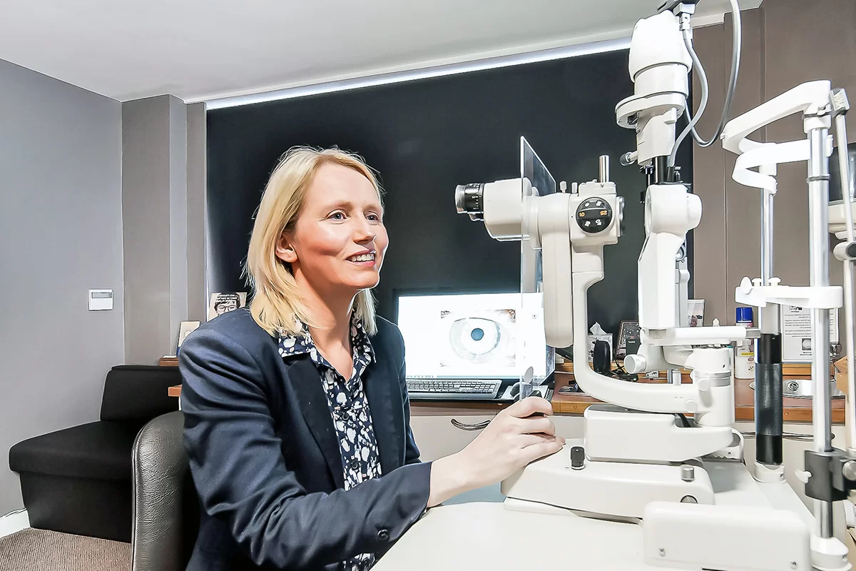 Smiling woman adjusting a slit lamp in an optometrist's office.