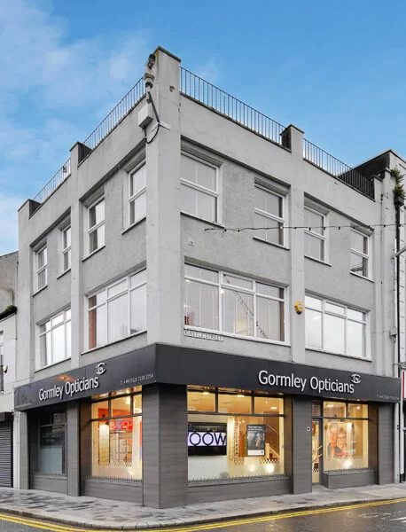 Corner building with large windows and signage reading 'Gormley Opticians' on both visible sides.
