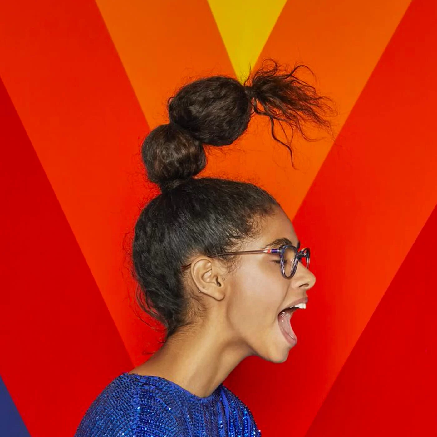 Side profile of a woman with glasses and a unique two-bun hairstyle, shouting against a vibrant red and orange geometric background.