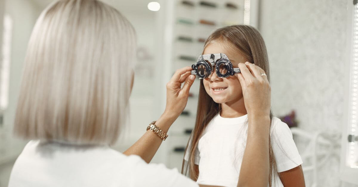 Optometrist adjusting a trial frame on a smiling young girl.