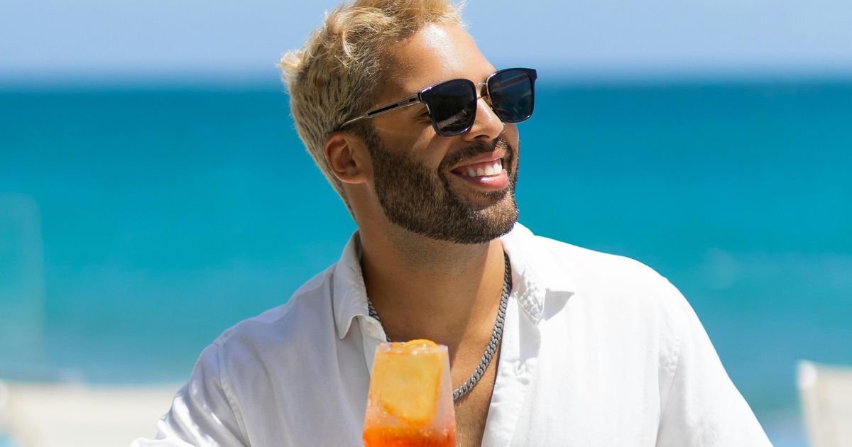 Smiling man wearing dark square sunglasses relaxing at the beach.