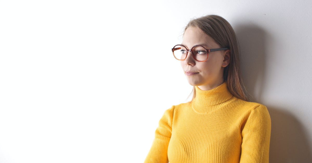Young woman wearing round tortoiseshell glasses in a yellow turtleneck.