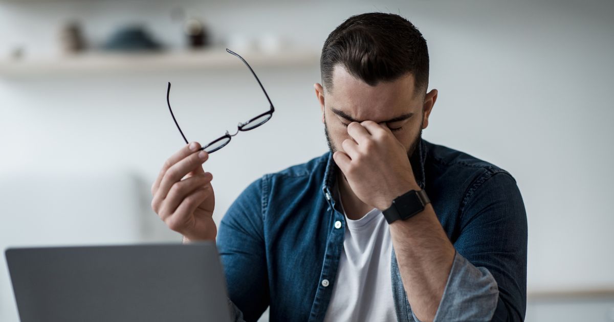 Man rubbing tired eyes while holding glasses at his laptop.