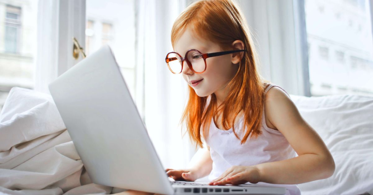 Young red-haired girl wearing round glasses using a laptop.