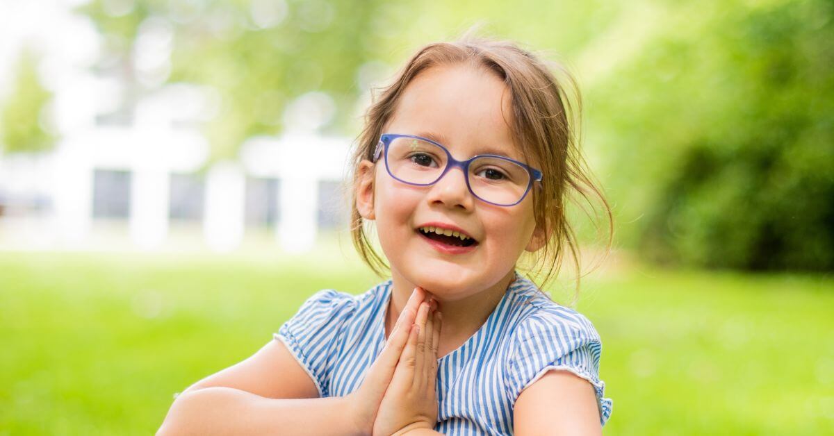 Happy young girl wearing blue glasses smiling outdoors in a park.