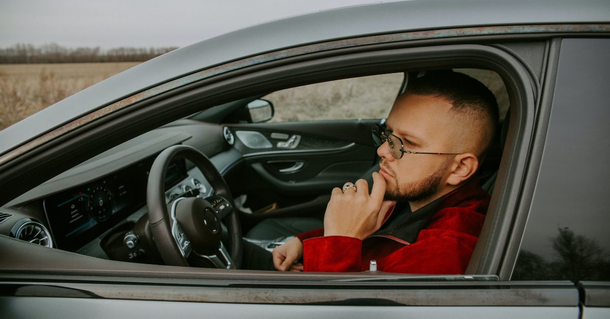 Man wearing small tinted sunglasses sitting in a car.