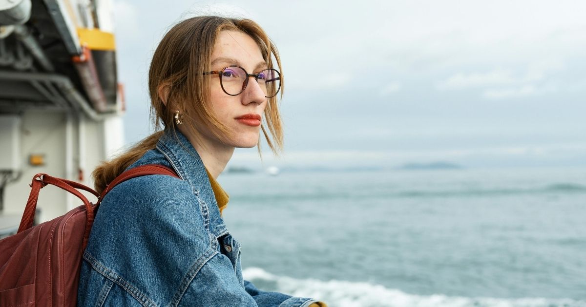 Young woman wearing round tortoiseshell glasses by the sea.
