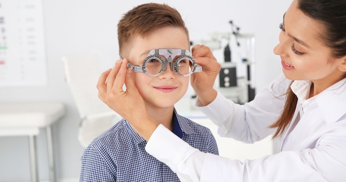 Female optometrist fitting a trial frame on a smiling young boy.