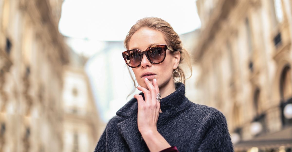 Woman wearing oversized tortoiseshell cat-eye sunglasses on a city street.