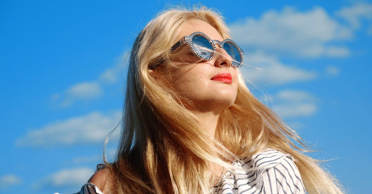 Woman wearing patterned heart-shaped sunglasses against a bright blue sky.