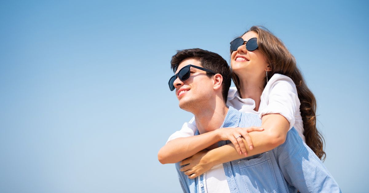Happy couple both wearing dark sunglasses outdoors against blue sky.