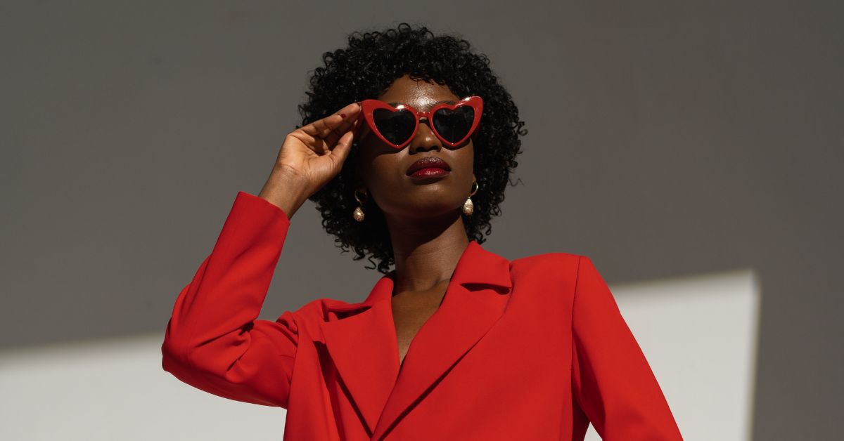 Woman in a red suit wearing bold red heart-shaped sunglasses.