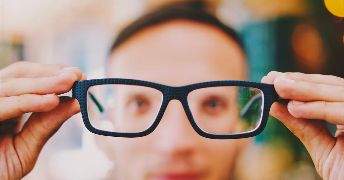 Person holding up black rectangular glasses frames toward camera.