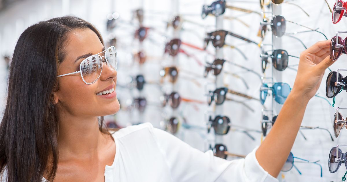 Woman trying on white aviator sunglasses while browsing an eyewear display.