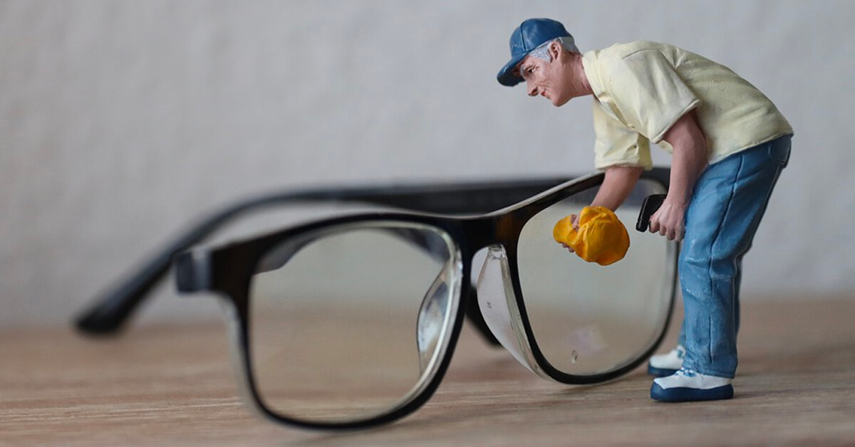 Tiny miniature figurine polishing a large glasses lens.