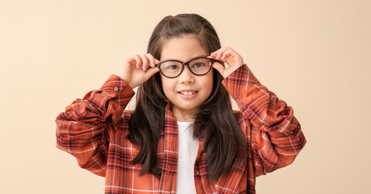 Smiling young girl adjusting her black glasses frames with both hands.