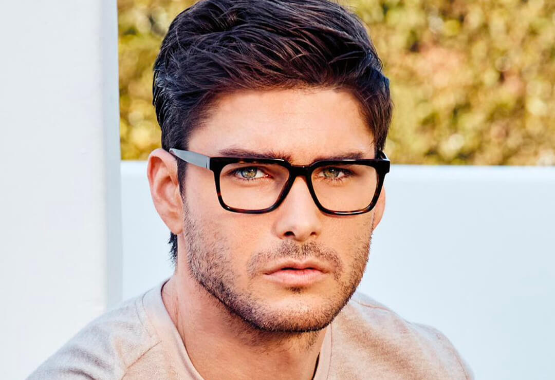 Man wearing bold dark square glasses frames, looking forward.