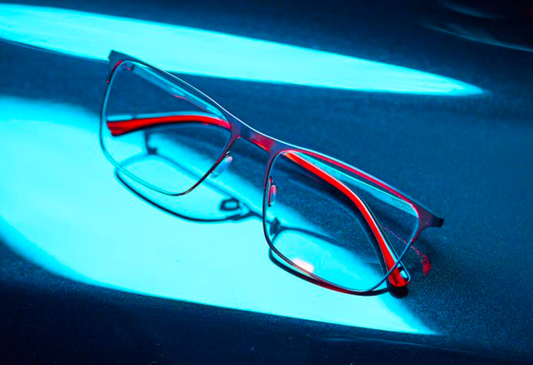 Red and black glasses frames under dramatic blue lighting.