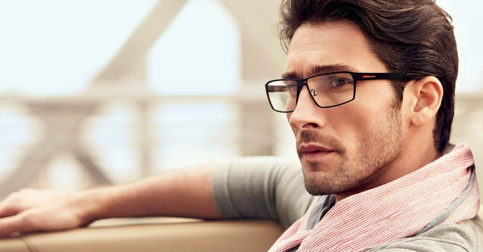 Man wearing Jaguar black rectangular glasses frames, gazing away.