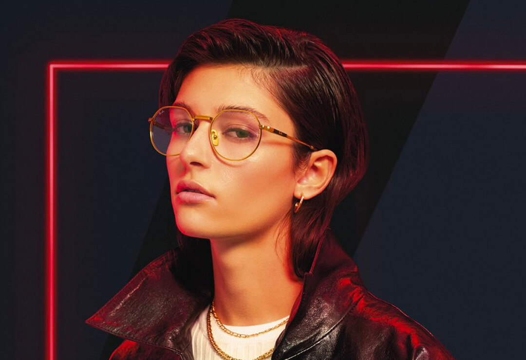 Person wearing rectangular Ray-Ban glasses against red background.
