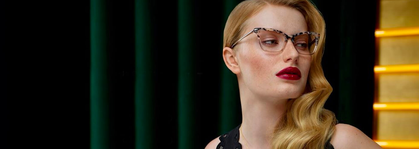 Woman wearing spotted cat-eye glasses in a glamorous editorial setting.