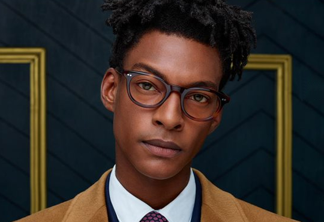 Man wearing brown Ted Baker glasses against gold background.