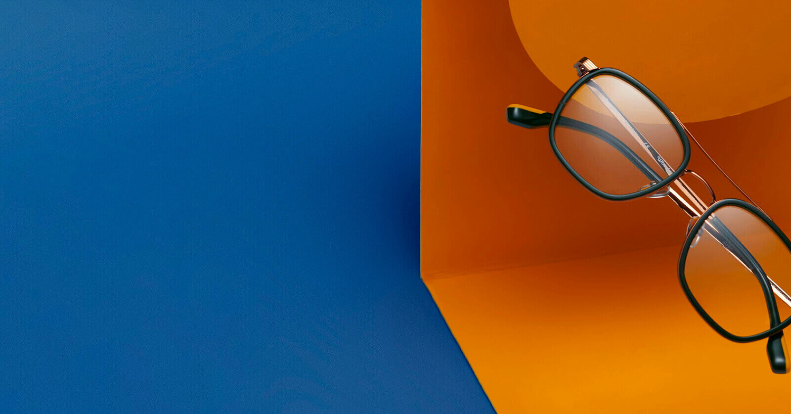 Green square Woodys glasses frames on bold orange and blue background.