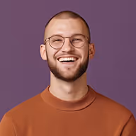 Smiling man with glasses, short hair, and beard wearing an orange sweater against a purple background.