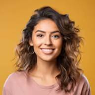 Smiling woman with curly brown hair wearing a pink top against a yellow background.