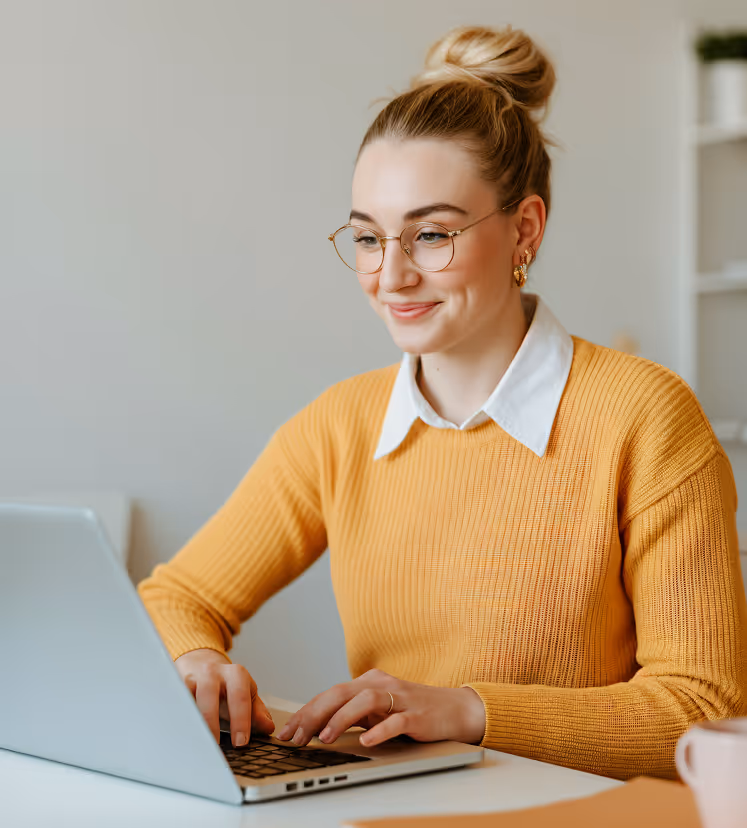 Man in white winter jacket and goggles crouching beside a Dalmatian dog wearing sunglasses and fluffy earmuffs in a snowy mountain landscape.