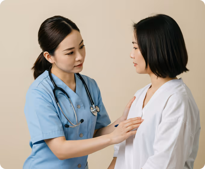 Female healthcare professional in blue scrubs examining a woman's chest during a medical checkup.