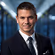 Smiling man in business suit and tie standing in a modern office hallway.