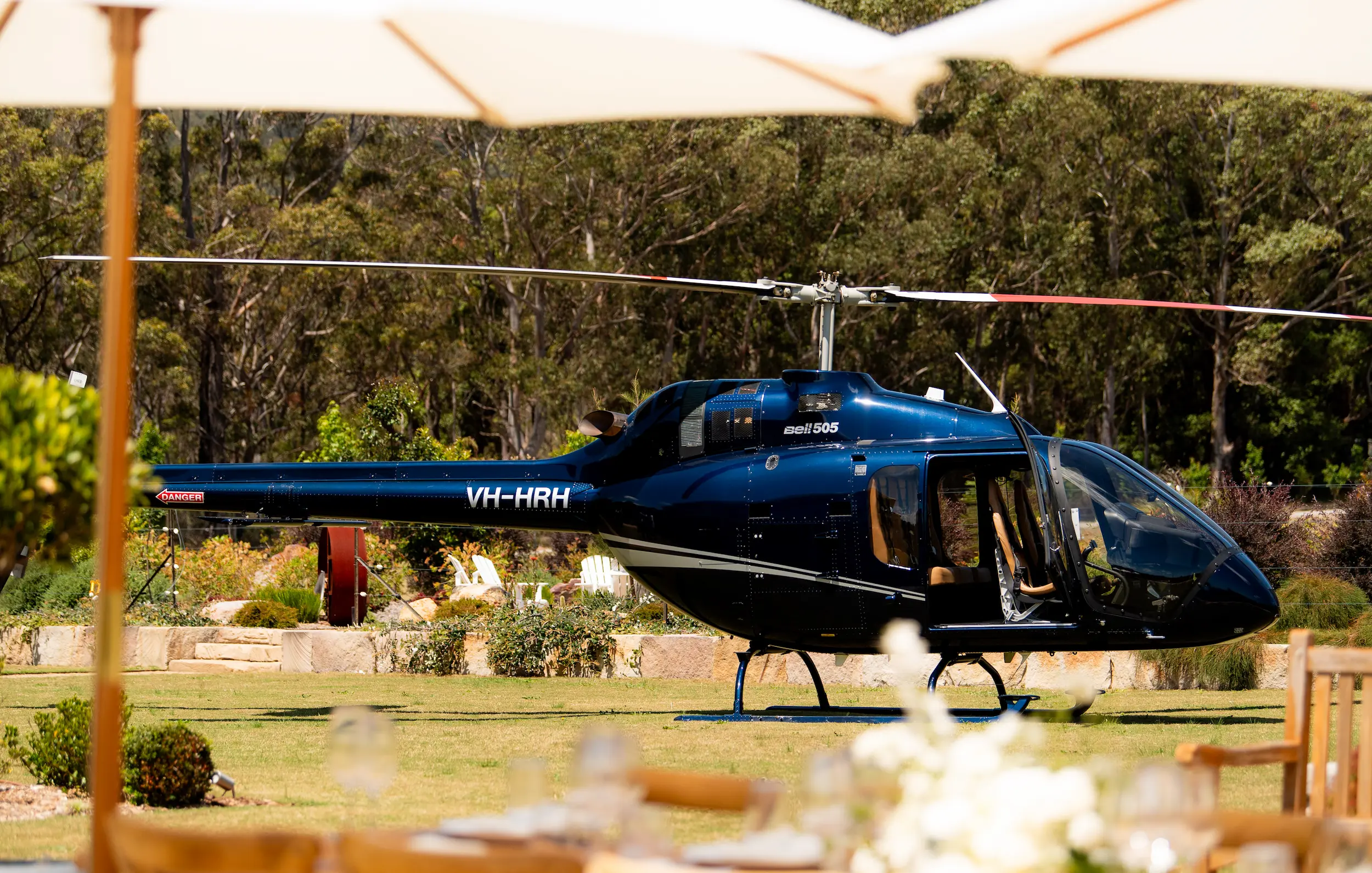 A helicopter is parked on the grass near a table and umbrellas.