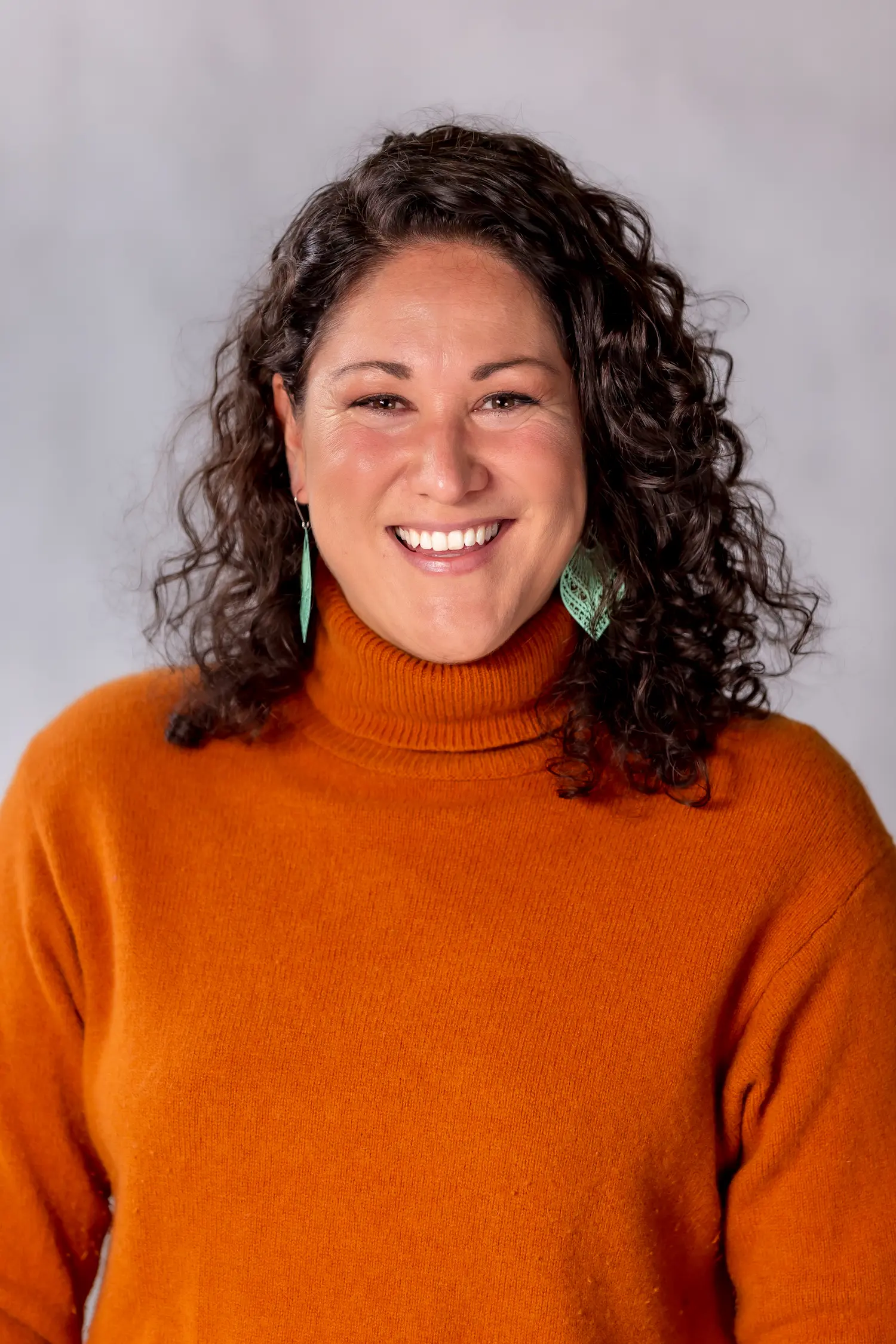 A woman with curly hair wearing an orange sweater.