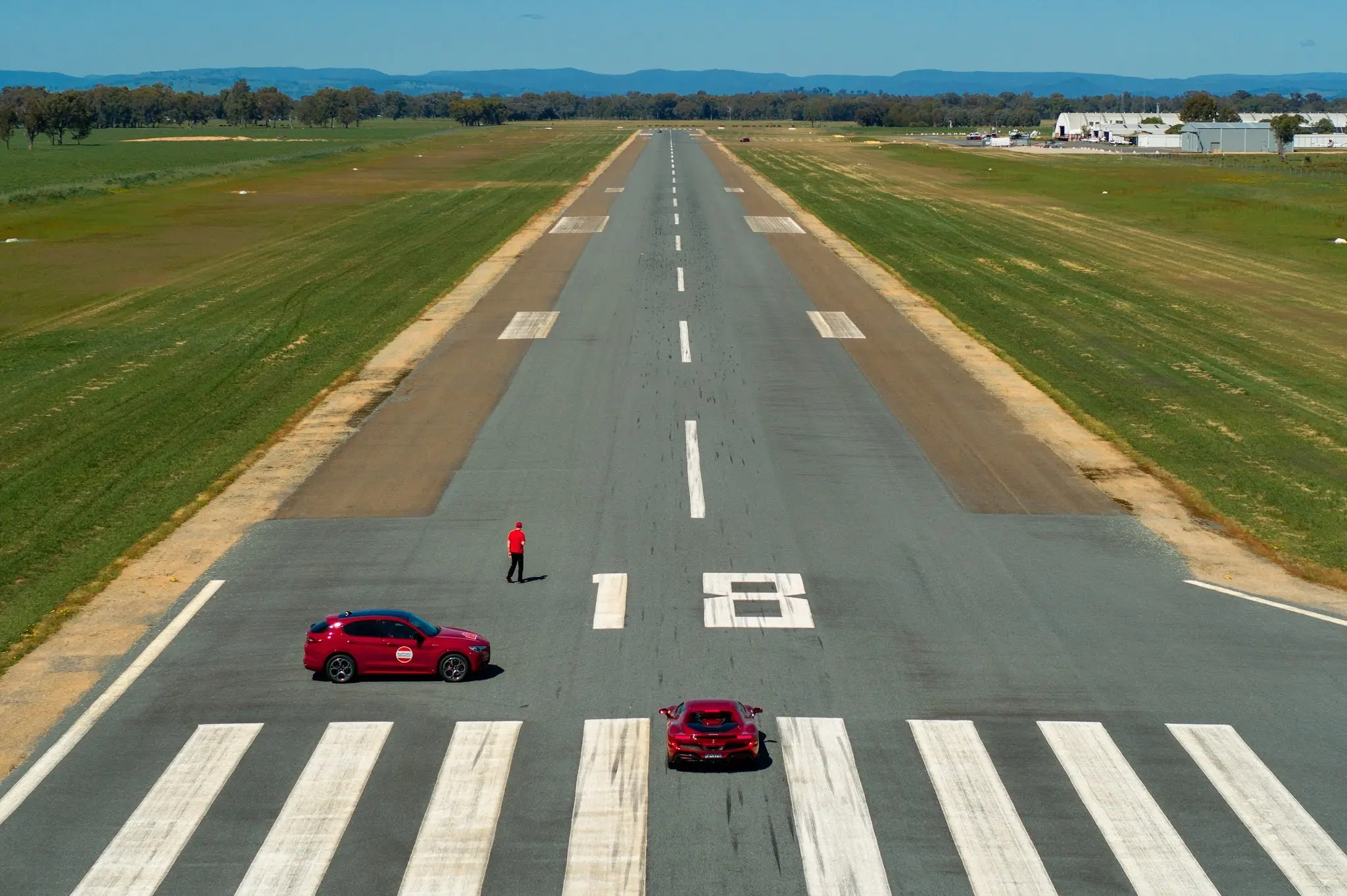 A red car driving down a road next to a field.