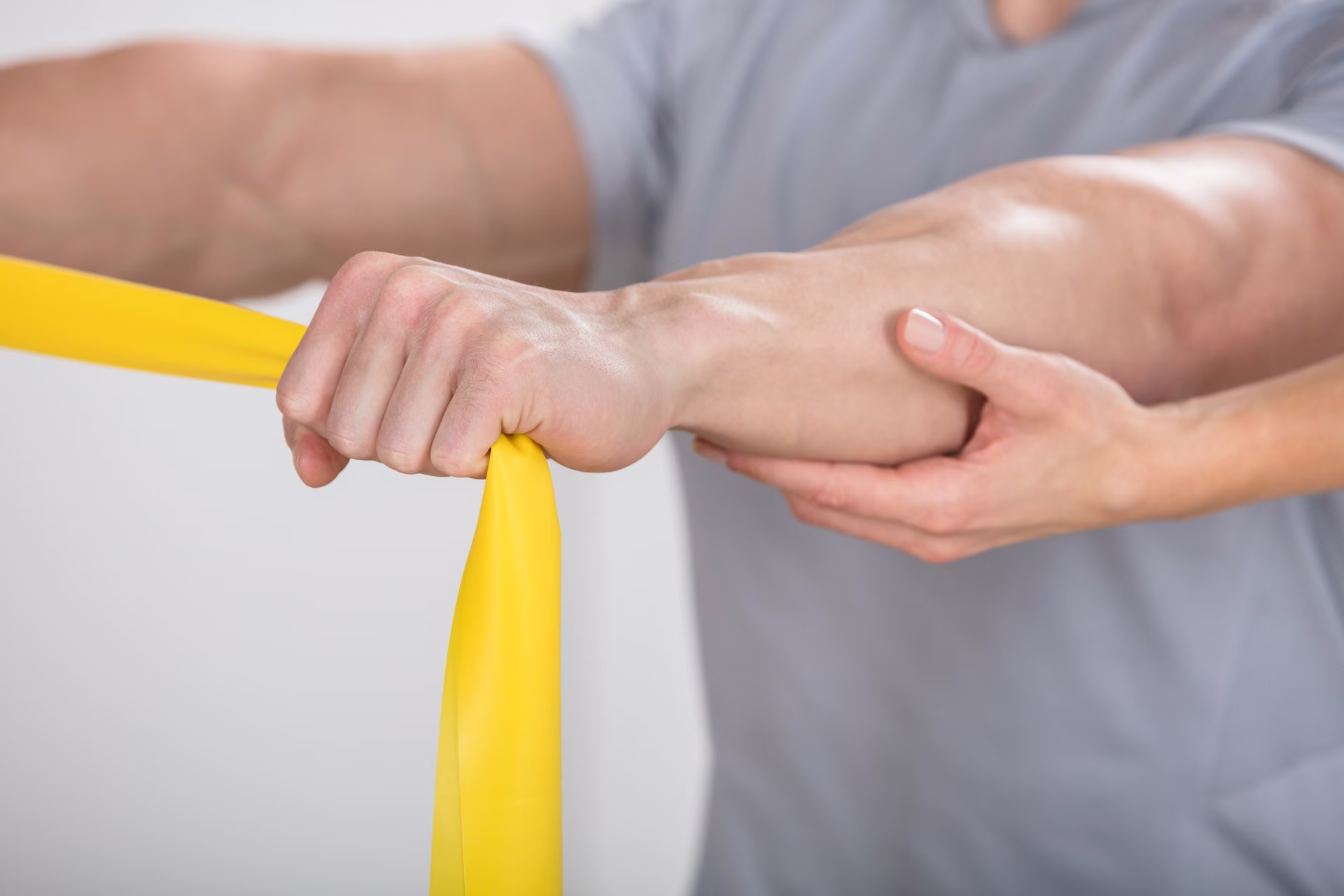 Physiotherapist supporting a patient's forearm during a resistance band exercise.