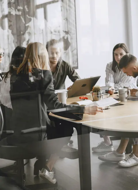 Group of five colleagues engaged in a meeting around a conference table with laptops and coffee cups.